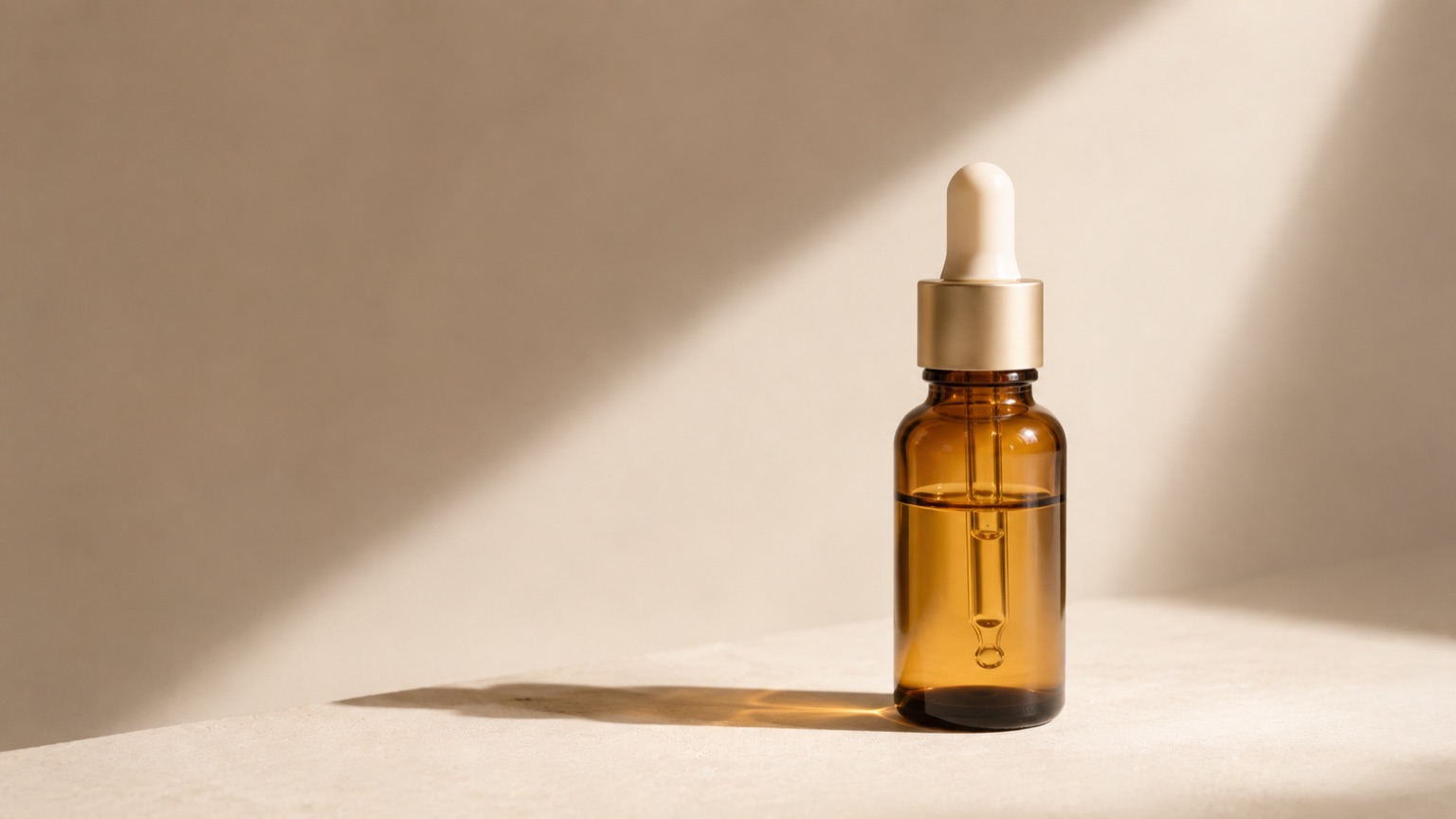 An amber glass dropper bottle of pale gold serum in a shaft of morning light.