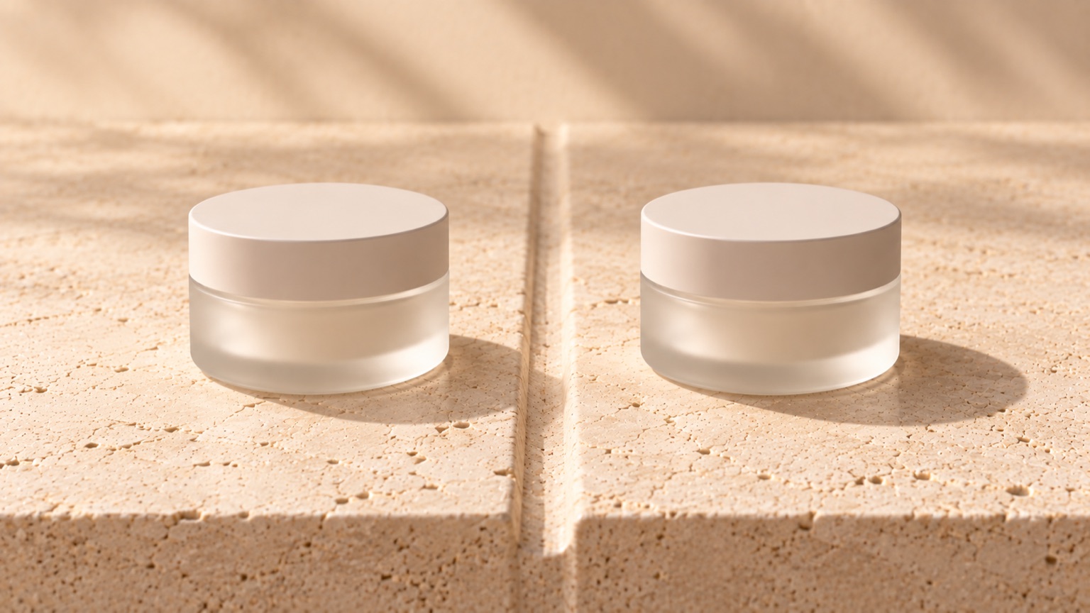 Two identical plain frosted jars placed symmetrically either side of a shallow groove in pale stone.
