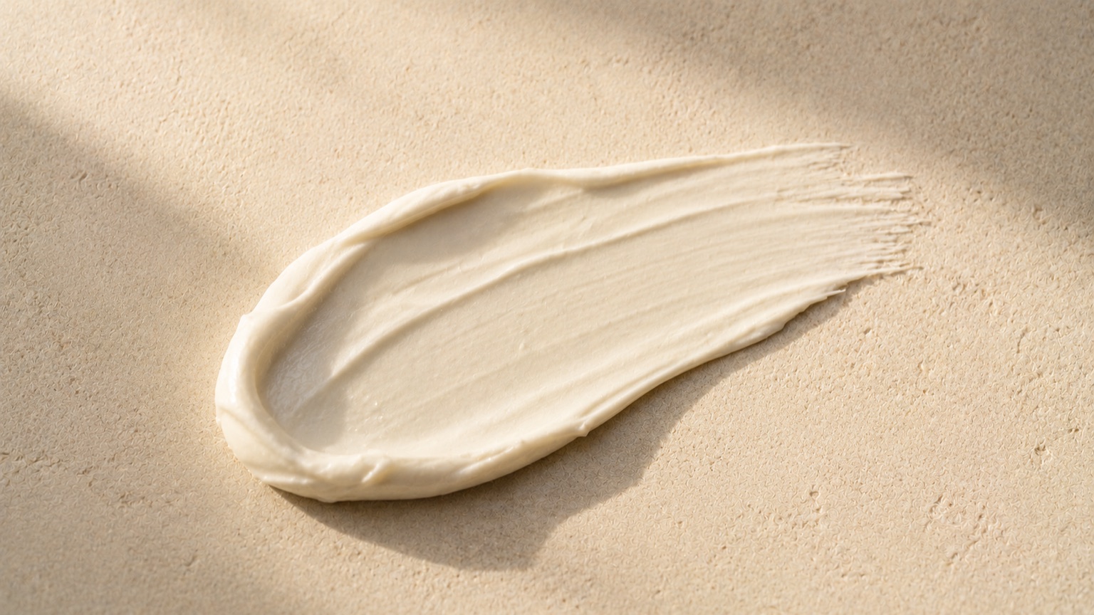 A thick cream smeared as a single swatch across a pale stone slab, its texture caught by raking light.