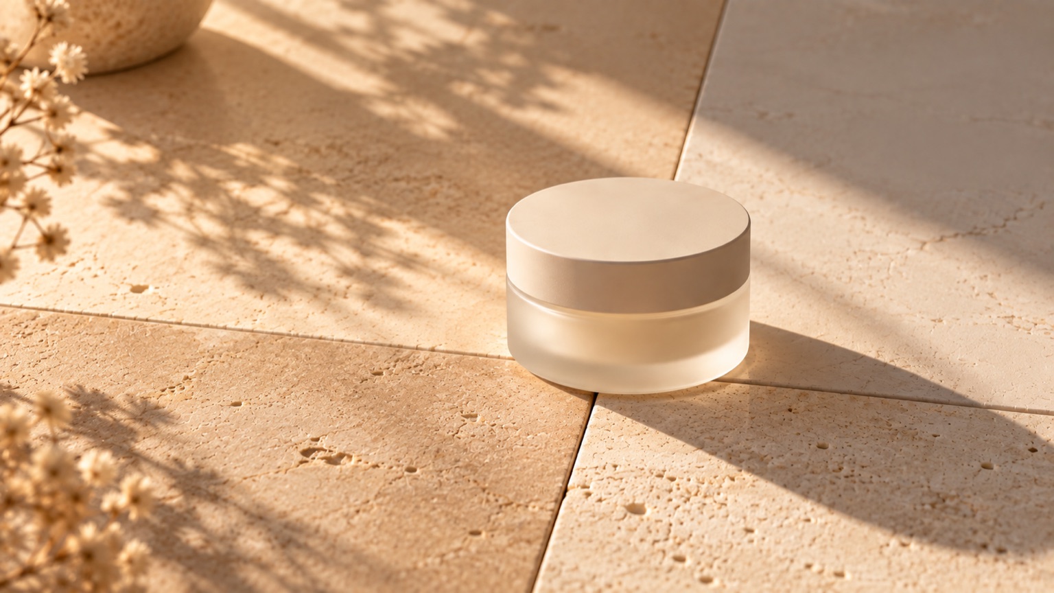 Four pale stone tiles of slightly different warmth laid edge to edge, a plain jar across one join.