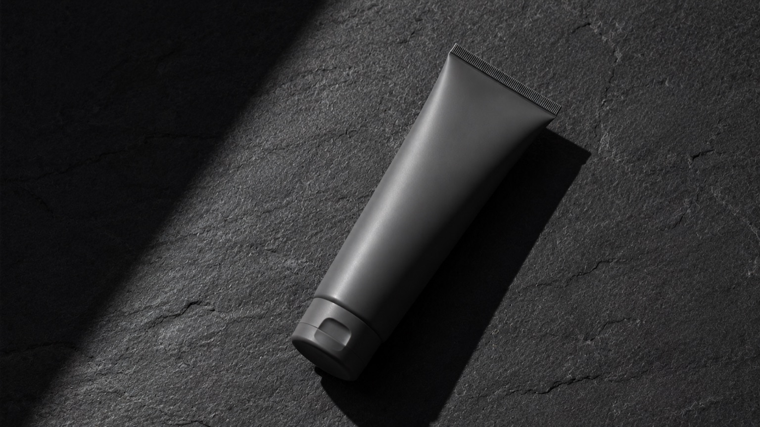 A charcoal grey plain tube lying on dark slate under stark directional daylight.