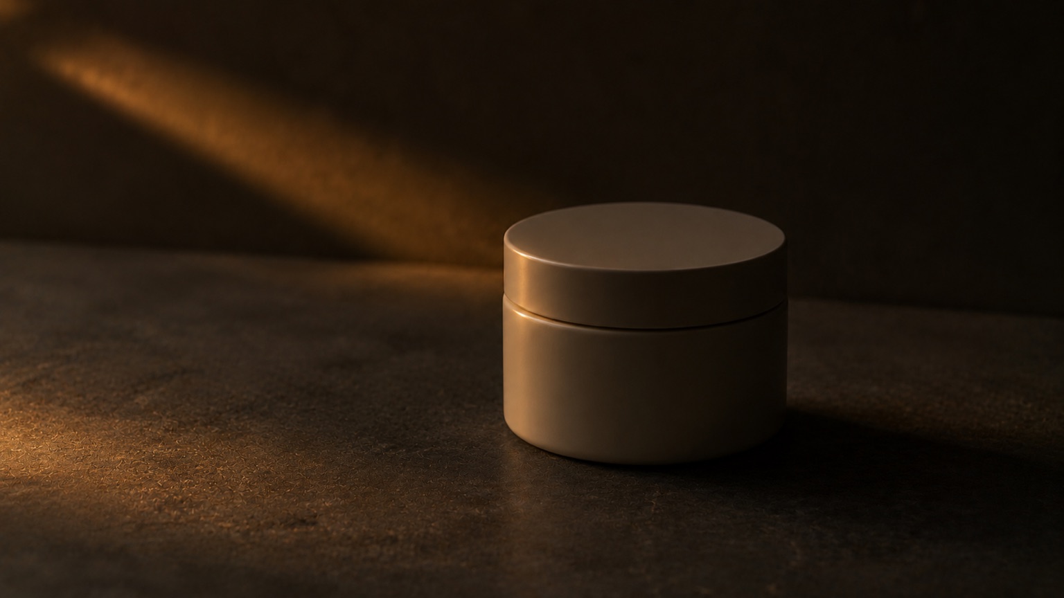 A closed round jar on dark stone at dusk, lit by a single amber highlight along its rim.