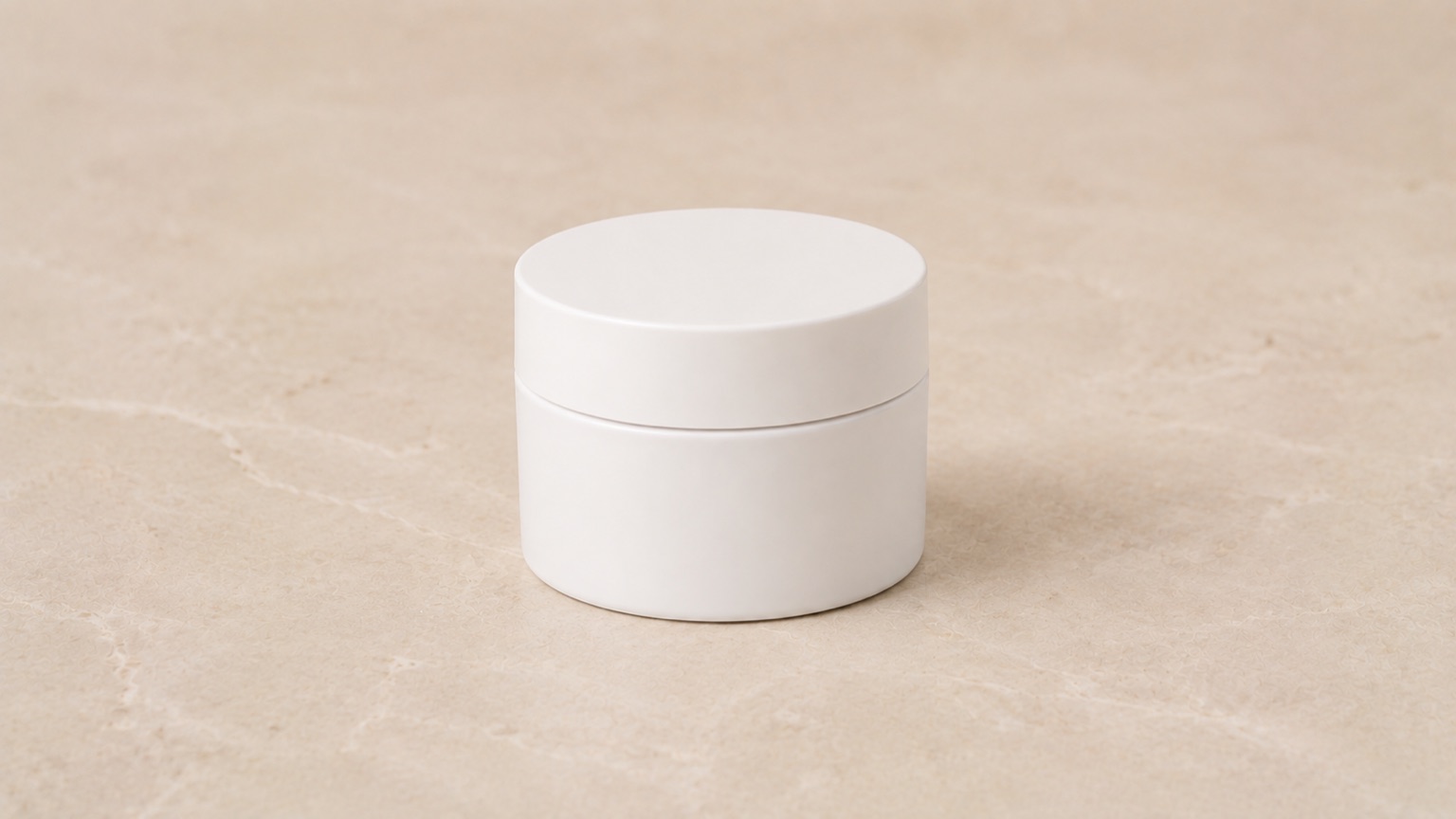 A single plain white jar standing on warm porcelain in neutral, even light.