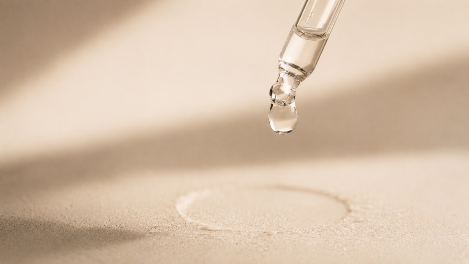 A single clear droplet hanging from the tip of a glass dropper above a ring of condensation.