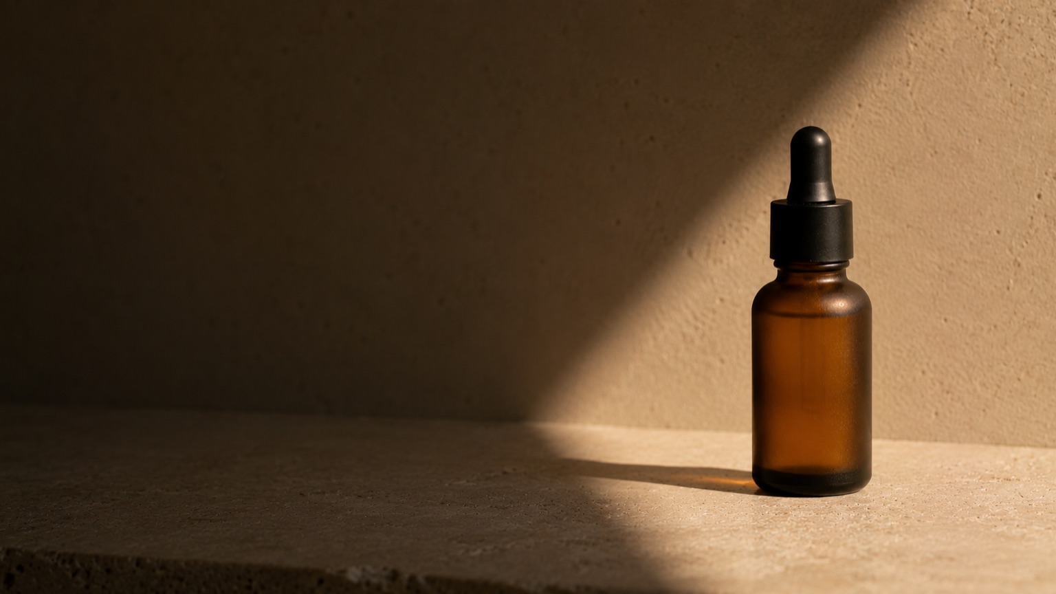 An amber-glass dropper bottle in low warm evening light, deep shadow filling most of the frame.
