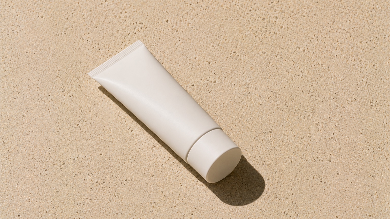 A plain unlabelled white tube on warm porcelain under hard overhead light casting one crisp shadow.