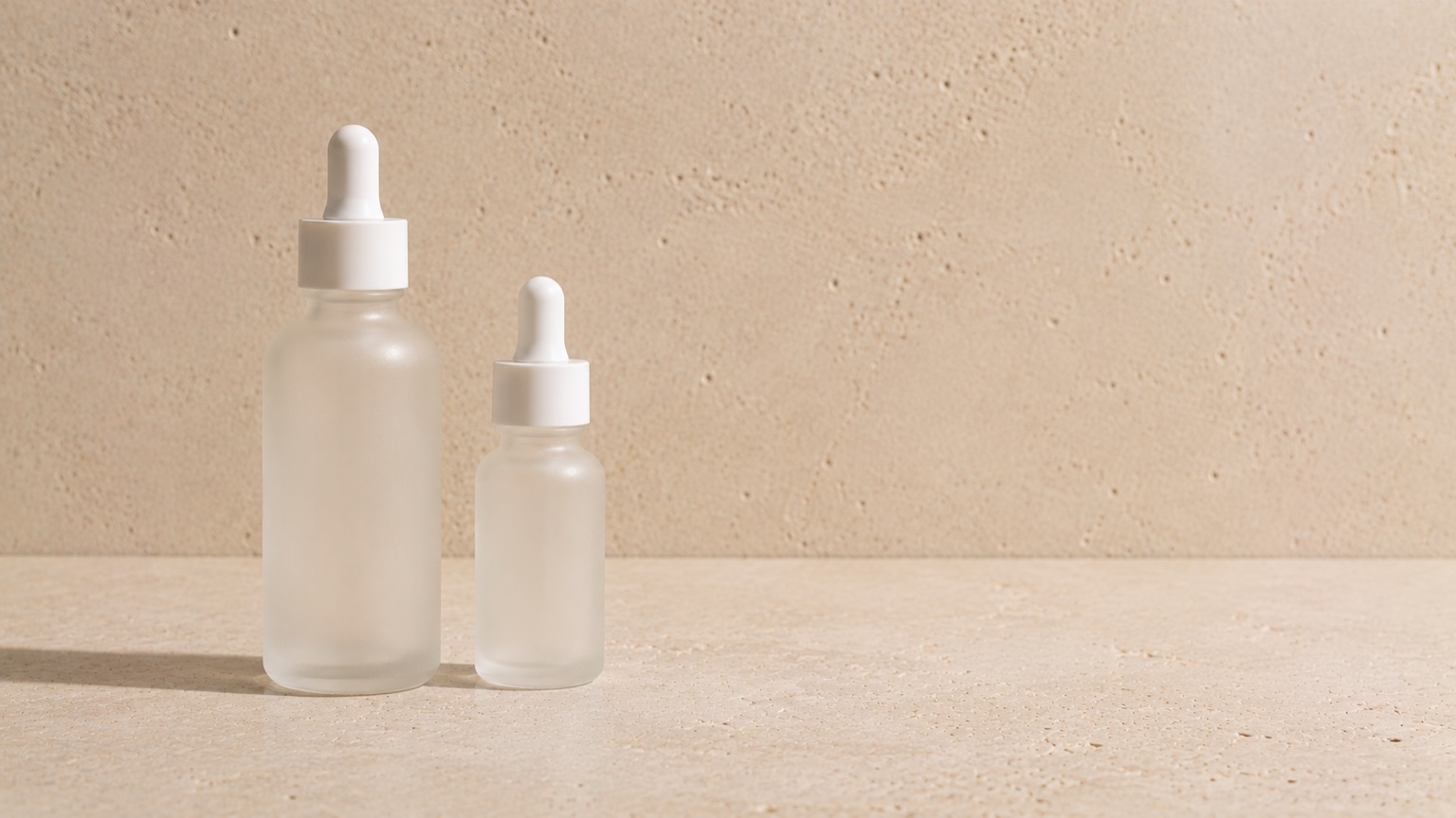 Two unlabelled dropper bottles of clearly different sizes side by side on pale stone in even daylight.